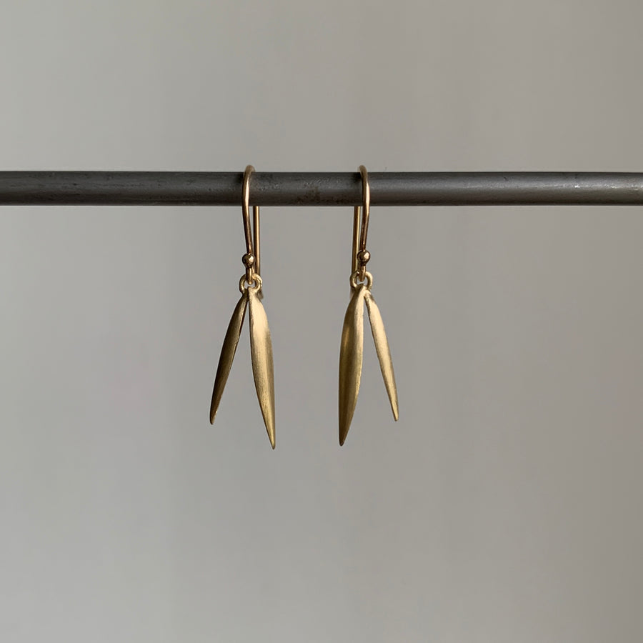 Gold leaf-shaped earrings hanging on a rod against a gray background