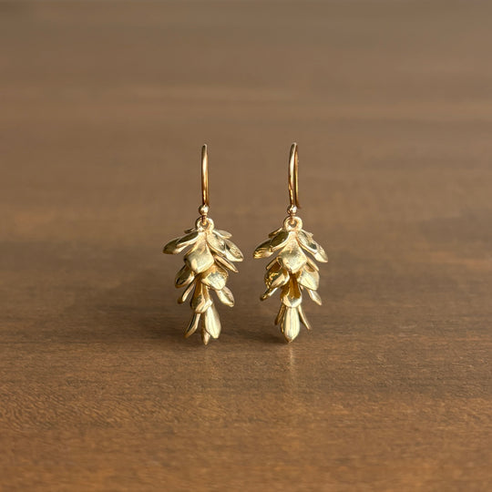 Gold leaf-shaped earrings on a brown background