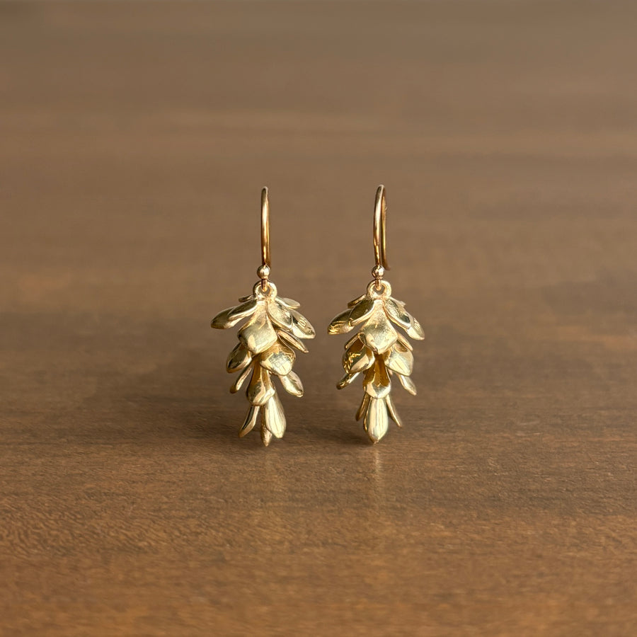 Gold leaf-shaped earrings on a brown background