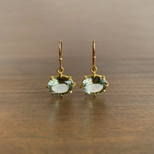 Gold earrings with green gemstones on a wooden surface