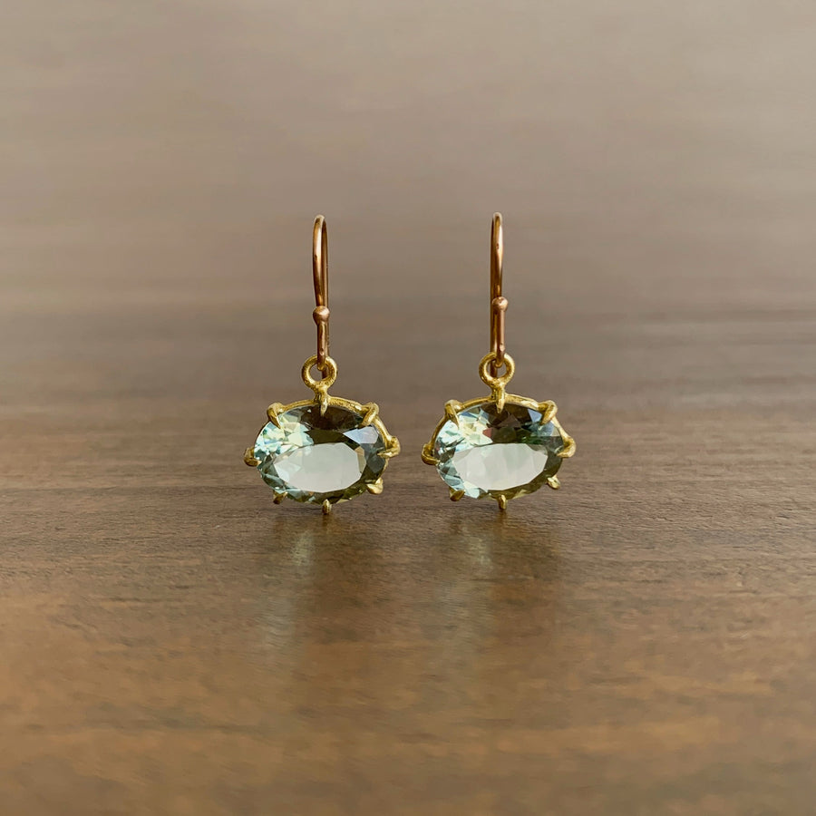 Gold earrings with green gemstones on a wooden surface