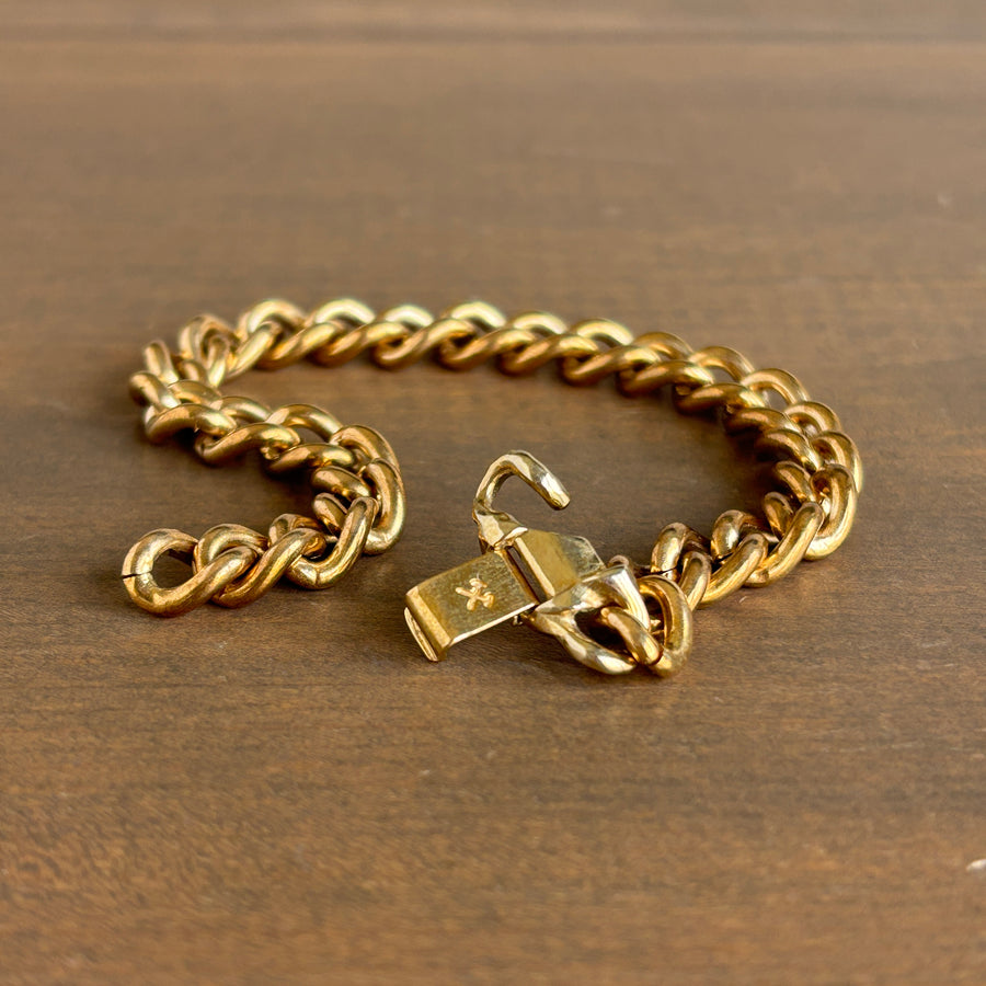 Gold chain bracelet with a padlock charm on a wooden surface