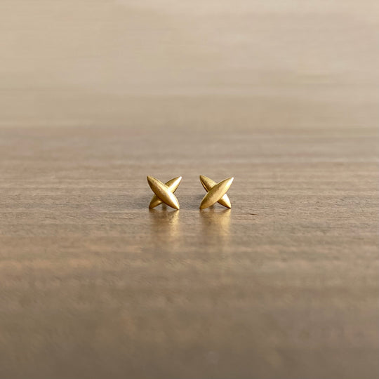 A pair of small star-shaped cross stud earrings in 18k yellow gold, placed on a wooden surface.