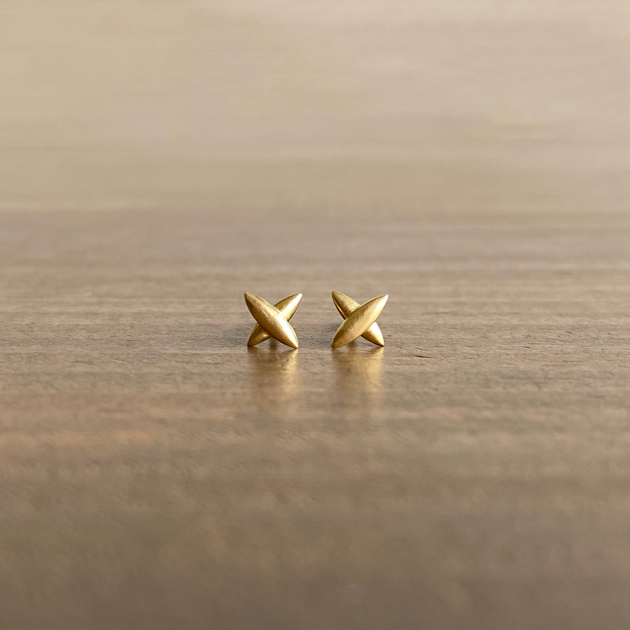 A pair of small star-shaped cross stud earrings in 18k yellow gold, placed on a wooden surface.