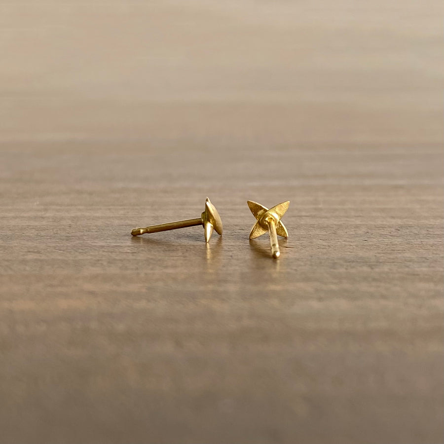 A pair of small star-shaped cross stud earrings in 18k yellow gold, placed on a wooden surface.
