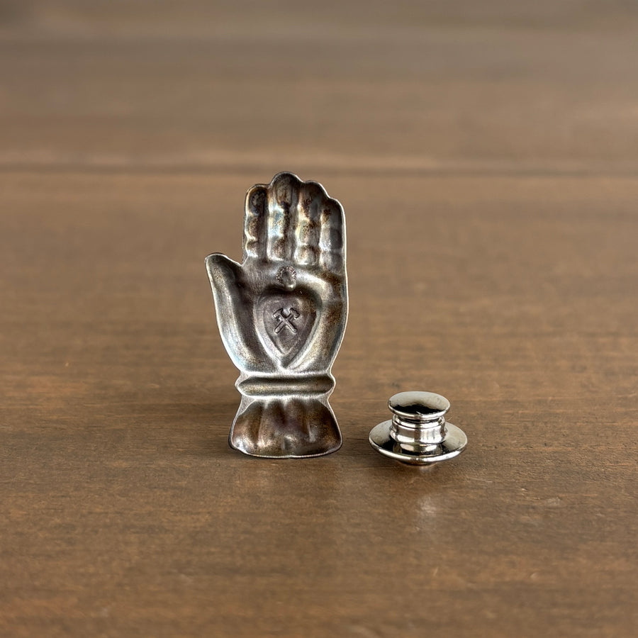 Silver hand-shaped pin with a small clutch on a wooden surface