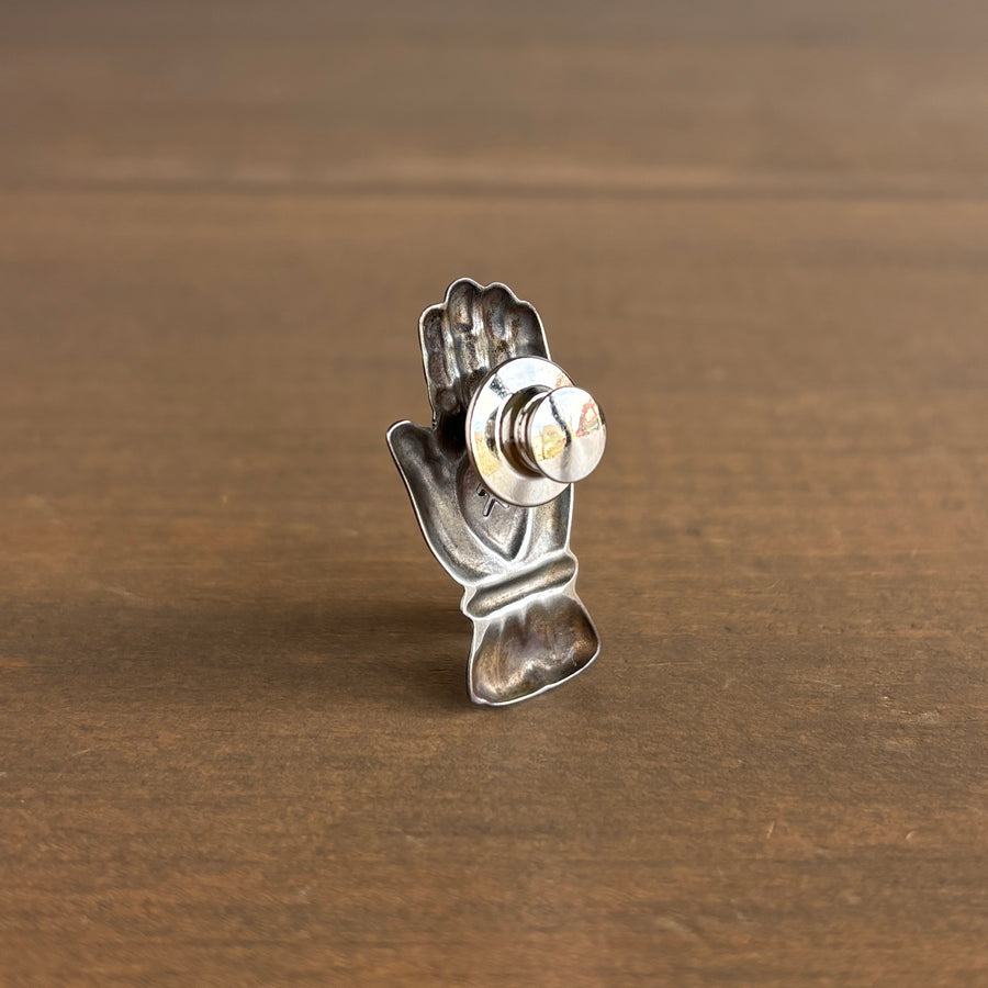 Metallic hand-shaped object with a central knob on a wooden surface