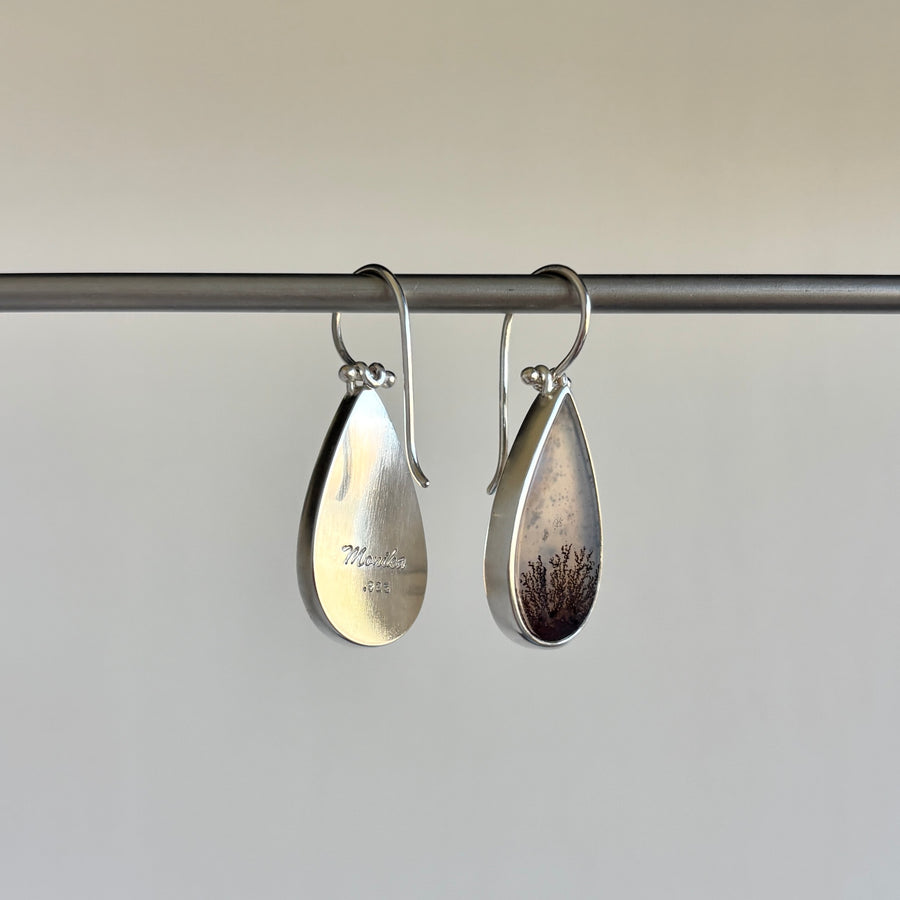 Pair of silver teardrop earrings on a rod with a neutral background