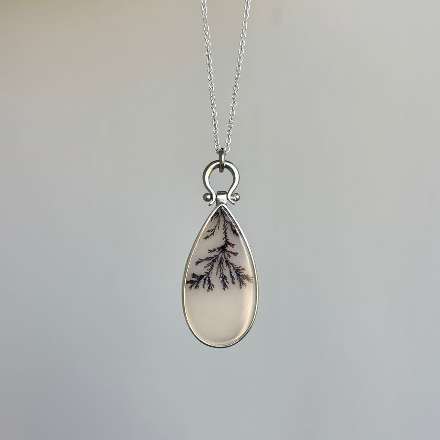 Teardrop-shaped pendant with dendritic pattern on a silver chain against a gray background
