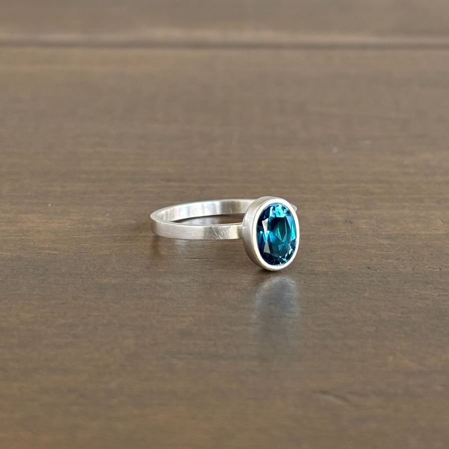 Silver ring with a blue gemstone on a wooden surface