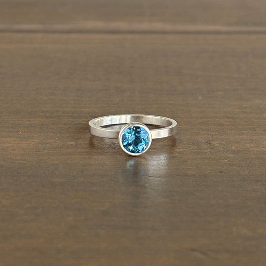 Silver ring with a blue gemstone on a wooden surface