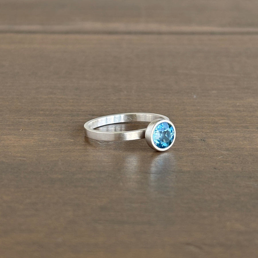Silver ring with a blue gemstone on a wooden surface