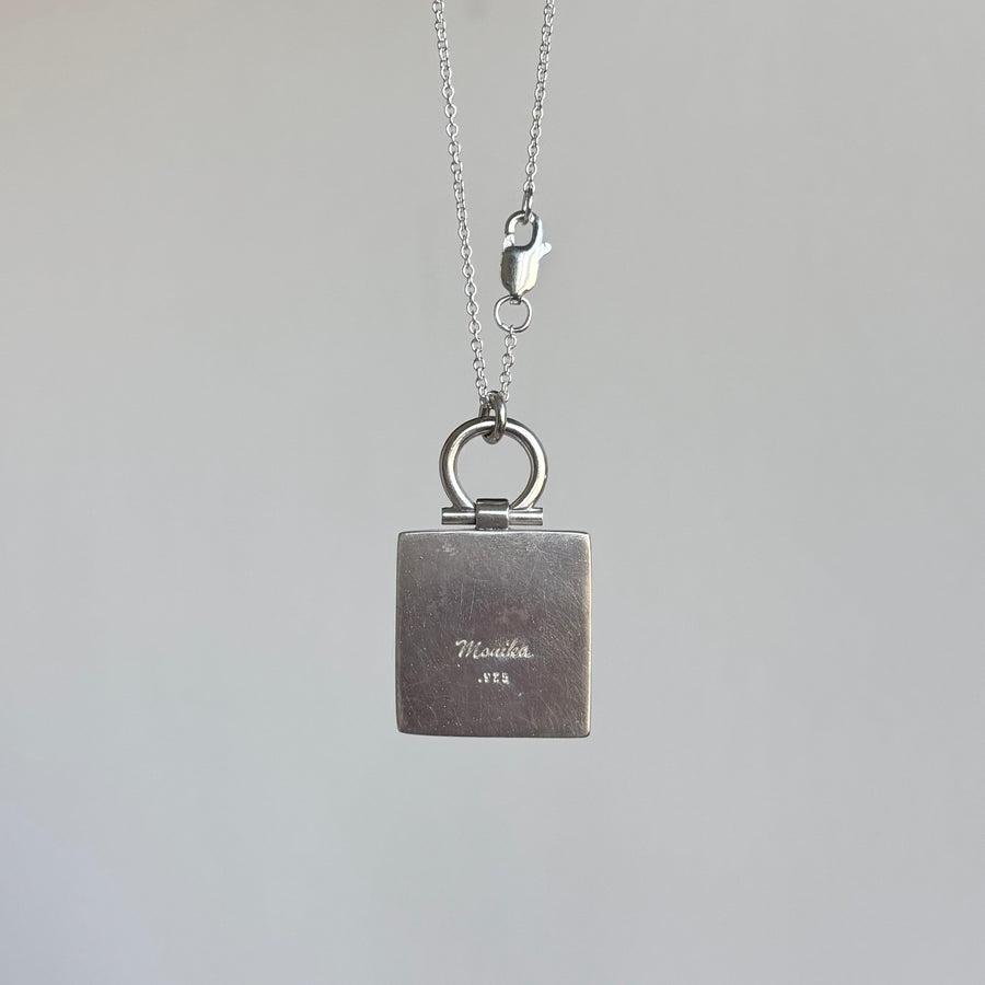 Silver necklace with a square pendant on a gray background