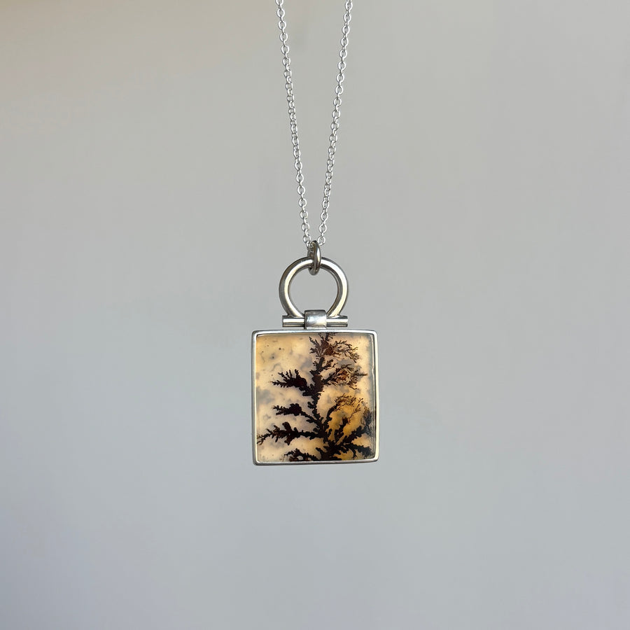 Square pendant with dendritic pattern on a chain against a gray background