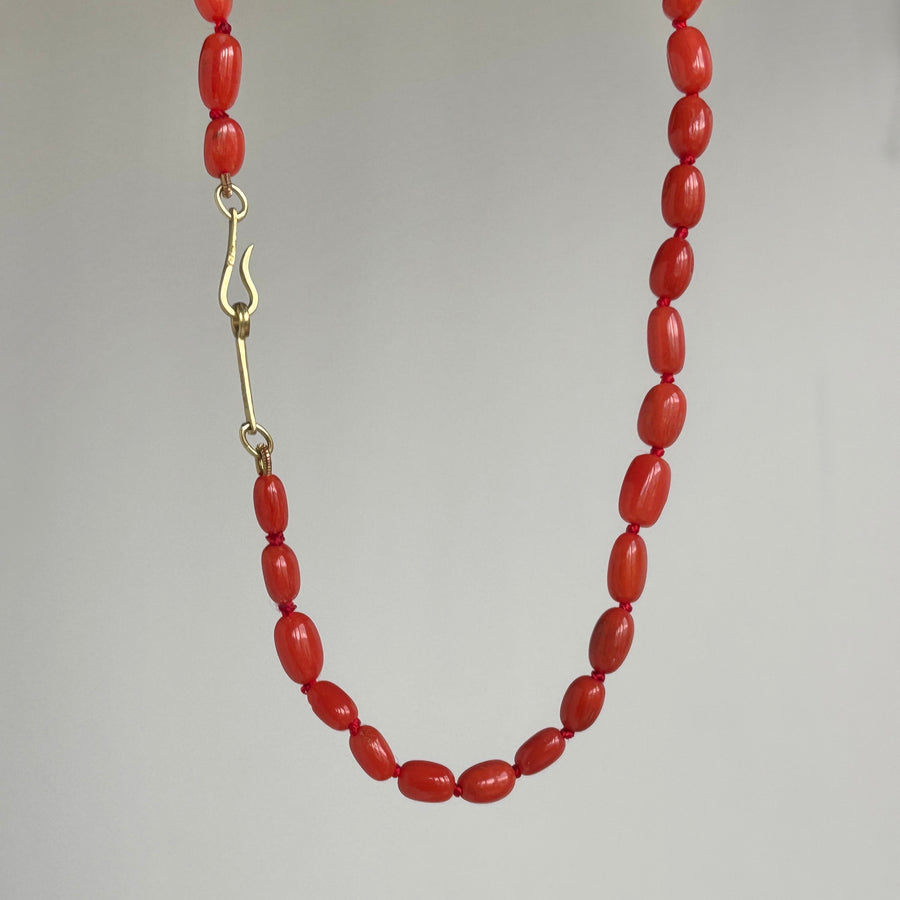 A red beaded necklace with polished oval beads and a gold-tone lobster clasp, shown against a neutral light gray background.