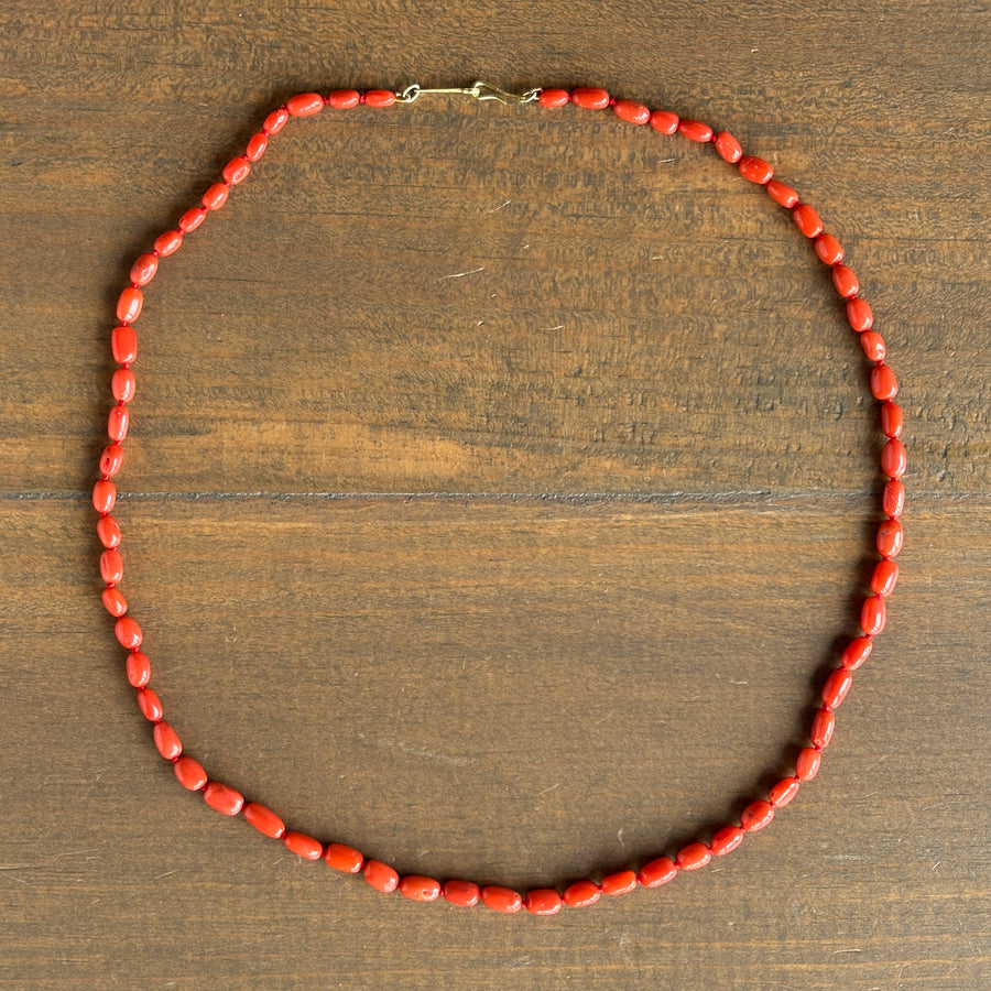 A red coral beaded necklace with a small gold clasp, arranged in a circle on a dark brown wooden surface.