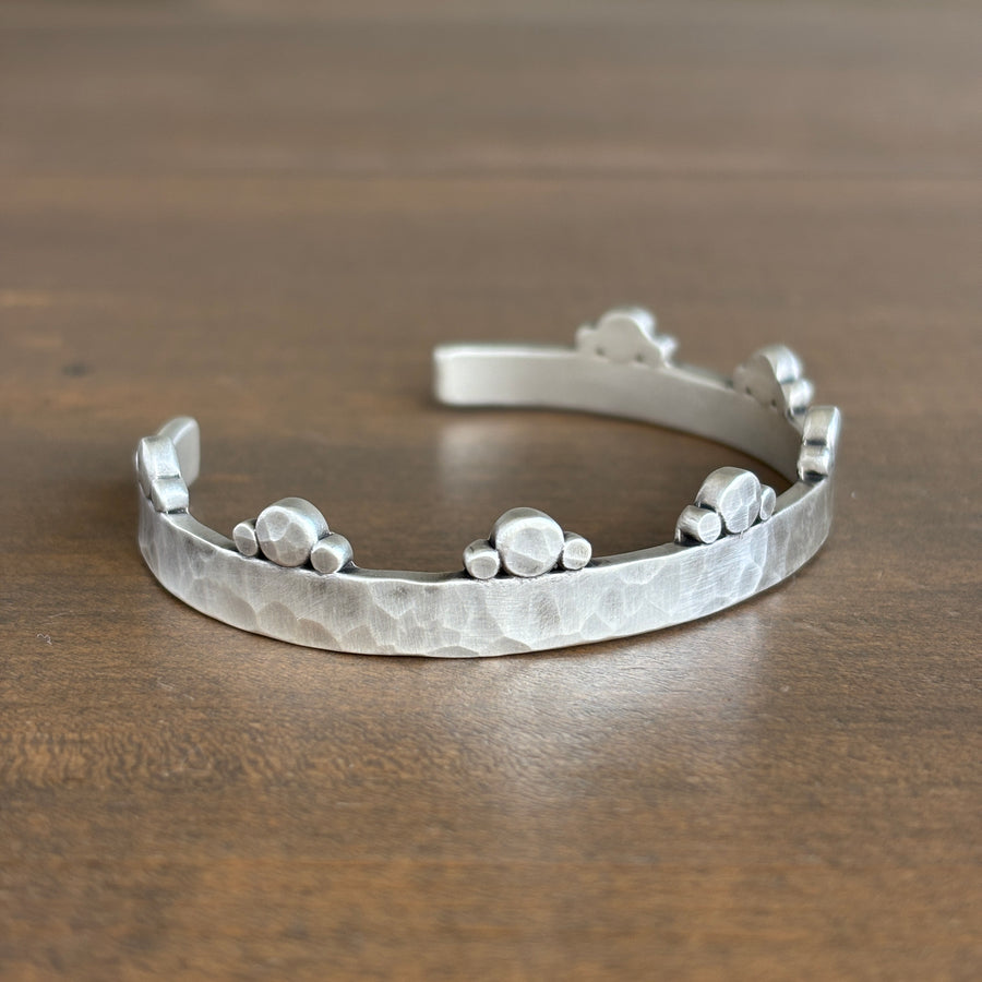 Silver bracelet with textured design on a wooden surface