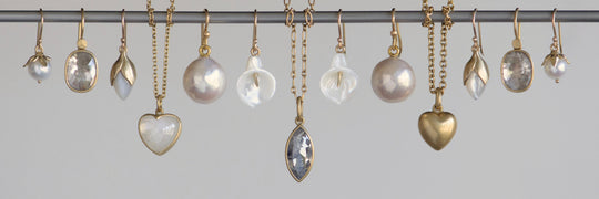 Collection of pearl and heart-shaped jewelry hanging on a rod against a light gray background